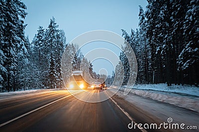 Cars drive with headlights on the winter road in a snow storm in the twilight when snow is flying. Concept of driving in Stock Photo