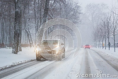 Cars moving on slippery snowy road at city street during heavy snowfall at evening in winter . Traffic obstacle due blizzard and Stock Photo