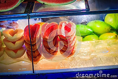 Cart of street fruit vendor with sliced papaya, melon, watermelon and mango on tray for sale on the street in Bangkok night mark Stock Photo