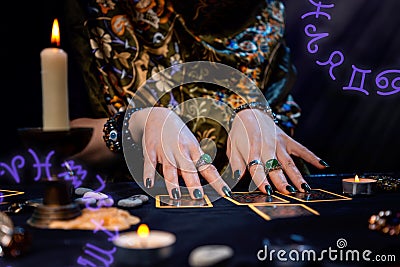 Cartomancy. A fortune teller reads Tarot cards. On the table are candles. Hands close up. Zodiac circles are located in Stock Photo