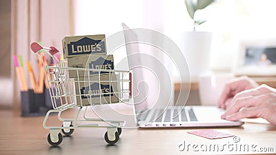 Cartons with LOWE`S logo in shopping trolley near customer with laptop. Editorial online shopping from home 3D rendering Editorial Stock Photo