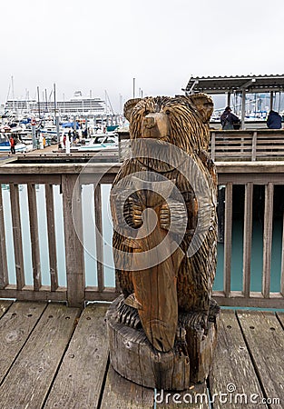 A carved bear holding a salmon on the boardwalk at the small boat harbour at Seward, Alaska with boats and cruise ship in Editorial Stock Photo
