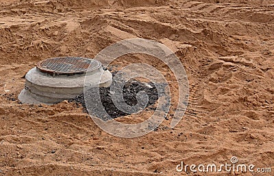 Cast-iron sewer hatch on a concrete base, located on mound of damp soil. Installation of water main and sewer well in the ground Stock Photo