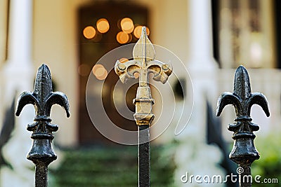 A cast wrought iron fence lined with black and gold fleur de lis post toppers with a New Orleans southern style home in Stock Photo