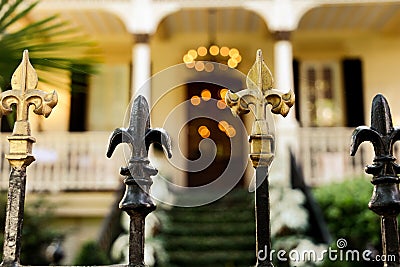 A cast wrought iron fence lined with black and gold fleur de lis post toppers with a New Orleans southern style home in Stock Photo