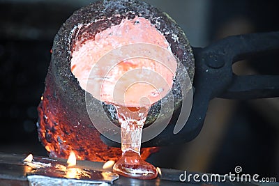 Casting liquid red hot metal from crucible held with tongs Stock Photo