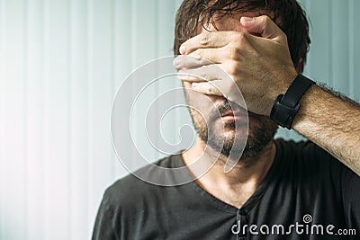 Casual adult male covering face and eyes with hand Stock Photo