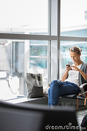 Casual blond young woman using her cell phone while waiting to board a plane Stock Photo