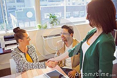 Casual business people shaking hands at desk and smiling Stock Photo