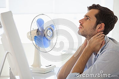 Casual businessman sitting at desk with electric fan Stock Photo