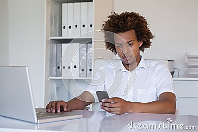 Casual businessman using his smartphone and laptop at his desk Stock Photo