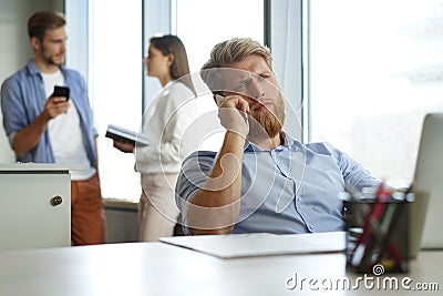 Casual businessman working at office desk, using mobile phone and laptop. Stock Photo