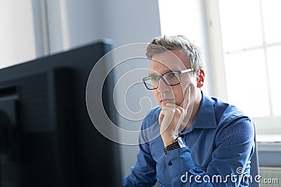 Casual businessman working in office, sitting at desk, typing on keyboard, looking at computer screen. Stock Photo