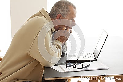 Casual dressed and anxious man biting his fingers as he looks at a computer screen. A pair of glasses lying on a pile of papers ne Stock Photo