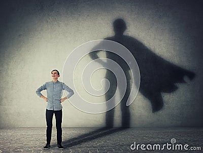 Casual teenage, keeps arms on hips smiling confident, casting a superhero with cape shadow on the wall. Student ambition success Stock Photo