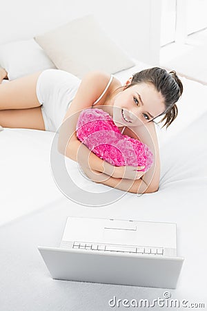 Casual woman with heart shaped pillow and laptop in bed Stock Photo