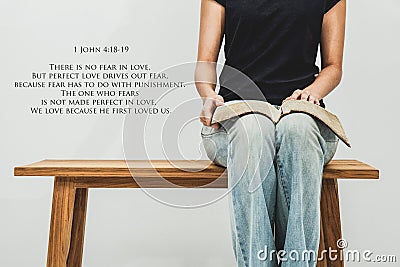 Casual young woman holds an open Bible 1 john 4:18-19 on her lap Stock Photo