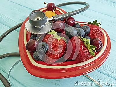 Cat homeless eats on the delicious strawberry, antioxid sweet blueberry, cherry, apricot plate heart on blue wooden, stethoscope Stock Photo