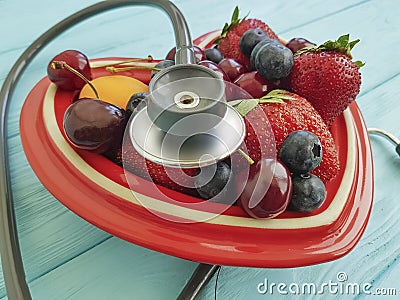 Cat homeless eats on the streetfruit strawberry, antioxid sweet blueberry, cherry, apricot plate heart on blue wooden, stethoscope Stock Photo