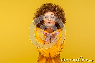 Catch my love kiss! Portrait of curly-haired young woman in urban style hoodie kissing air over palms Stock Photo