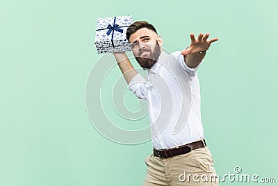 Catch your gift! Young adult man swung and wants to throw off your gift box, isolated on light green background. Stock Photo