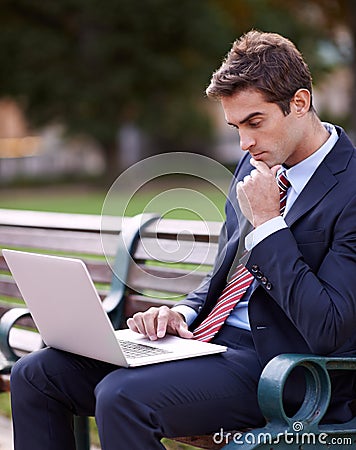 Catching up on emails at the park. a handsome businessman working on his laptop while sitting on a park bench. Stock Photo