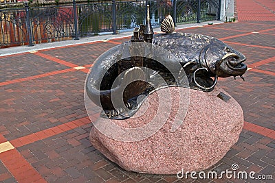 A catfish statue with a bridge Keeper`s booth on a large pink stone near a High bridge on the Pregol river embankment paved with g Editorial Stock Photo