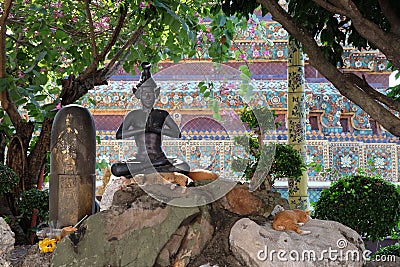 Cats have a rest near the sculpture of a meditating person in the territory of a Buddhist monastery Stock Photo