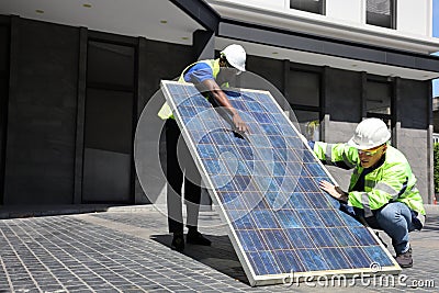 Caucasian and African American workers working on installing solar panel on the rooftop of the house for renewable energy and envi Stock Photo