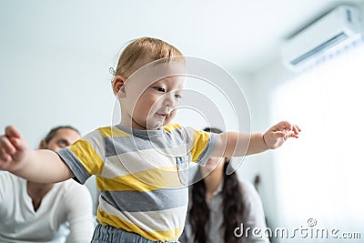 Caucasian baby boy child learn to walk with parents support in house. Happy family, mother and father helping young toddler son Stock Photo
