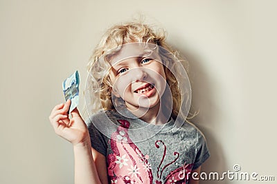 Caucasian blonde girl showing her missing tooth in mouth and holding money from tooth fairy. Proud child kid showing lost tooth. Stock Photo