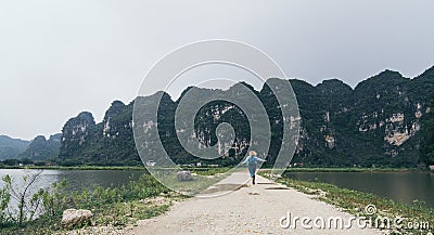 Caucasian blonde woman running towards limestone mountains in Ninh Binh province, Vietnam Stock Photo