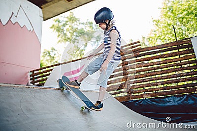 Caucasian boy in a helmet does tricks on a skateboard on a playground for skateboarding outside. A child skateboarder rides a Stock Photo