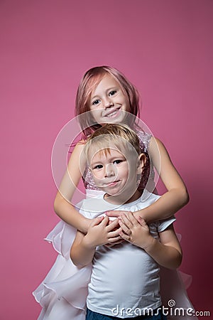 Caucasian brother and sister ,hugging on camera on pink background studio shot. Stock Photo