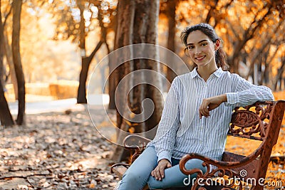 Caucasian brunette woman sitting on bench in natural park in autumn Stock Photo