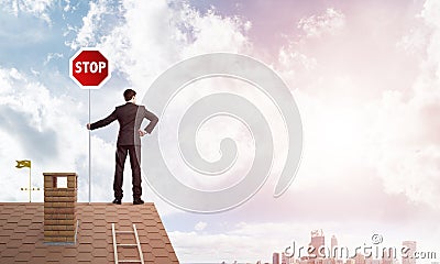 Caucasian businessman on brick house roof showing stop road sign. Mixed media Stock Photo