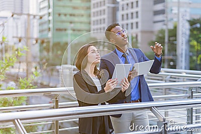 caucasian businesswoman in black suit and businessman in blue suit working together and looking at copy space outside building in Stock Photo