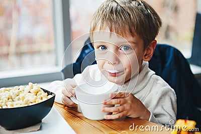 Caucasian child kid boy drinking milk from white cup eating breakfast lunch Stock Photo