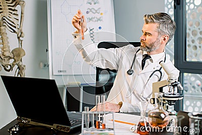 Caucasian concentrated male scientist doctor working in lab, doing research and making experiment, holding test tube Stock Photo