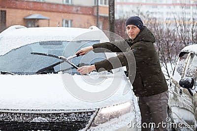 Caucasian driver cleans windshield and removes snow from rubber wipers of his car Stock Photo