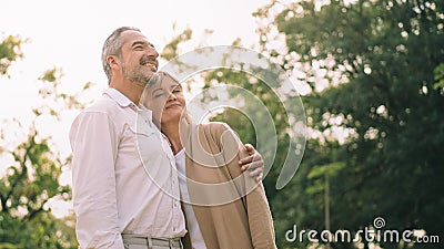 Caucasian elderly couple is standing, holds each other and smiling upward enjoy spending time together with happiness, a happily Stock Photo