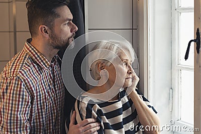 caucasian elderly pensioner mother and her middle-aged son worried looking through the window at a serious accident Stock Photo