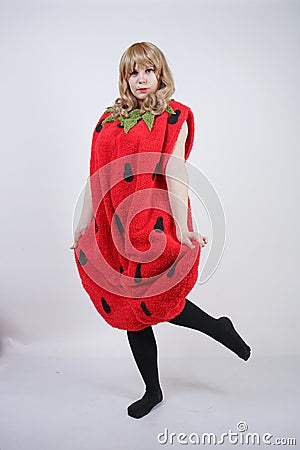 Caucasian emotive blonde girl in a huge plush suit of red strawberry on a white background in the Studio Stock Photo