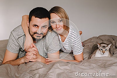 Caucasian family man and woman lying on bed in bedroom at home with oriental cat. Proud smiling pet owners with a domestic animal Stock Photo