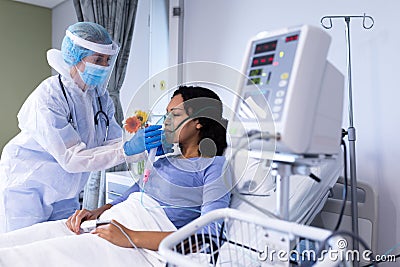 Caucasian female doctor in ppe suit checking african american female patient with ventilator Stock Photo