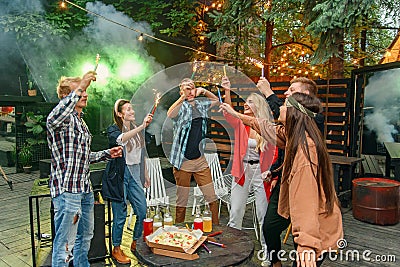 Caucasian friends having garden party outside, they dancing to the Dj`s music with bengal lights in house backyard at Stock Photo