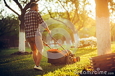 Caucasian Gardener working with lawnmower and cutting grass during summer season Stock Photo