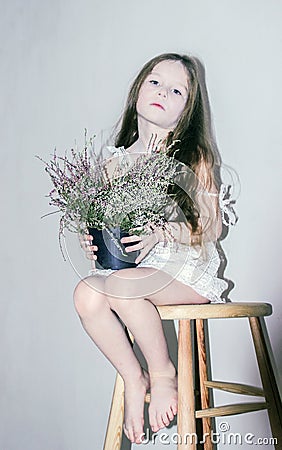 Caucasian girl leaned on a wooden chair in a white dress on a white background Stock Photo