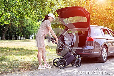 The caucasian girl puts the baby stroller in the trunk of the car. The concept of a spacious trunk in a family car. Stock Photo
