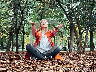 Caucasian girl with red gabardine plays on the ground with autumn leaves Stock Photo